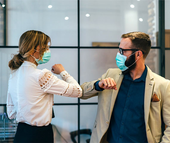 Two coworkers with masks greeting each other by bumping elbows